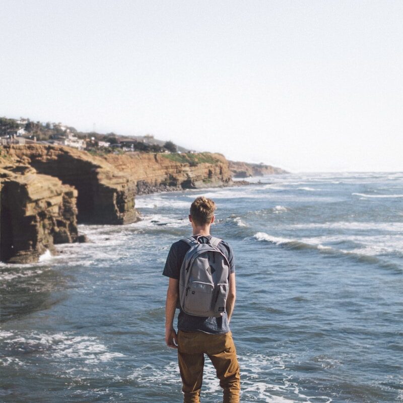 man standing on cliff looking at body of water